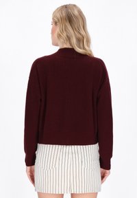 Burgundy neulepusero, jossa on lyhyt malli ja ribbitekstuuri, pitkät hihat ja pyöreä kaula-aukko. Takakuvassa esitelty.