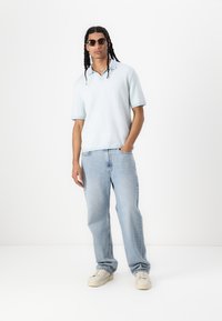 Ανοιχτό μπλε κοντομάνικο πόλο με υφή, συνδυασμένο με ανοιχτό μπλε τζιν και κρεμ αθλητικά παπούτσια. Αξεσουάρ: σκούρα γυαλιά ηλίου.