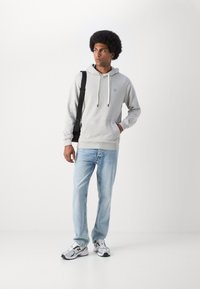 Grijze hoodie met een voorzak, witte trekkoorden, gedragen met lichtblauwe jeans en grijze New Balance sneakers. Eenvoudig ontwerp, casual pasvorm.