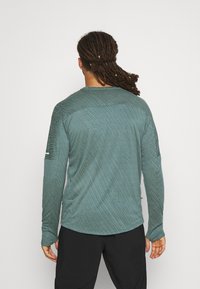 Long-sleeve, textured shirt in muted teal, featuring a crew neck and a subtle striped pattern across the back and shoulders.