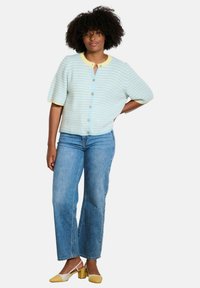 Light blue and white striped knit cardigan with short sleeves, featuring a yellow collar and button closure, paired with blue jeans and two-tone heels.