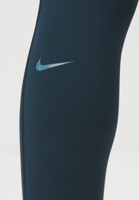Mornarske atletske tajice napravljene od rastezljivog materijala s glatkom teksturom, s reflektirajućim Nike logotipom blizu bedra i detaljem s patentnim zatvaračem.