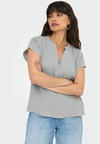 Top grigio a maniche corte con scollatura a barca e tessuto texturizzato. Abbinato a jeans azzurri chiari, con una vestibilità rilassata e gamba dritta.