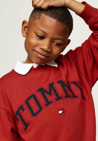 Felpa rossa con colletto bianco, con la scritta "TOMMY" in evidenza in blu navy. Tessuto morbido, design informale, con accento del logo blu e bianco.