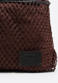 Brązowa torba na ramię z siateczki o teksturowanym, diamentowym wzorze. Posiada czarną skórzaną metkę z tłoczonym logo marki.