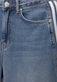 Jean en denim bleu clair avec une coupe classique, comprenant un design à cinq poches, des garnitures en métal argenté et des bandes latérales blanches contrastantes.