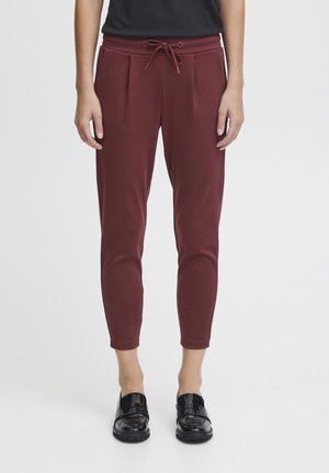 Burgundy tapered joggers with drawstring waistband, pocket details, and smooth texture, paired with black glossy shoes.
