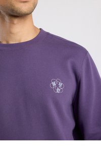 Paarse trui met ronde hals, voorzien van een klein, lichtgrijs logo op de borst. Gladde textuur en een casual pasvorm.