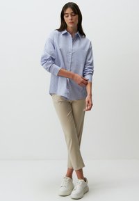 Blauw-wit gestreepte button-up overhemd met lange mouwen, gecombineerd met beige broeken en witte sneakers. Glad materiaal, klassieke kraag, relaxte pasvorm.