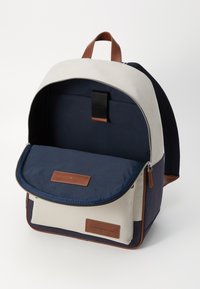 Zaino con un esterno in tessuto color crema e blu marino, dettagli in pelle, chiusura con zip e un interno spazioso e imbottito.