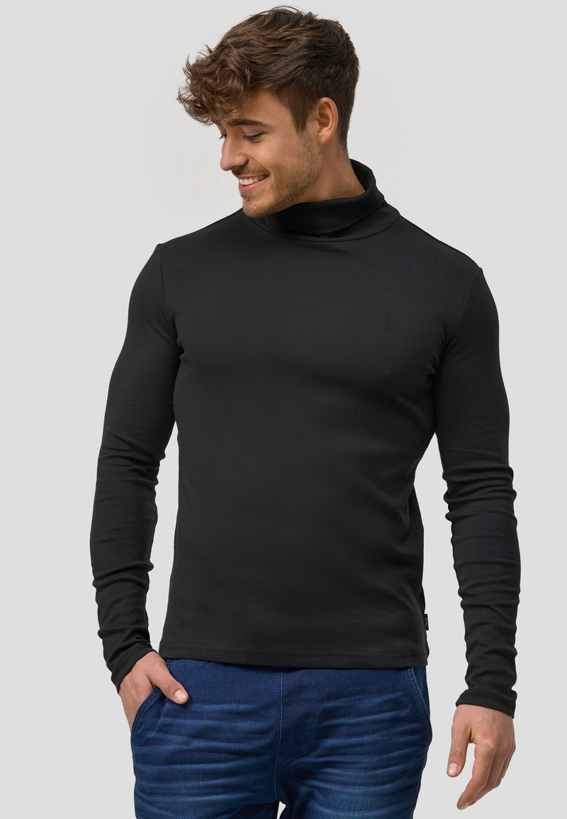 Svart långärmad polotröja i ett mjukt tyg, figurnära design med en diskret logotyp på bröstet och uppvikta ärmar.