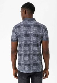 Kortærmet polo-shirt i mørkeblåt stof med et tekstureret geometrisk mønster i lysere nuancer, med krave og en afslappet pasform.