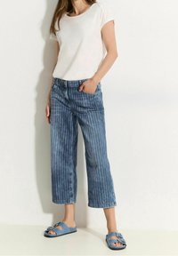 Top blanco de manga corta, jeans de pierna ancha a rayas en azul claro y sandalias azules con detalle de hebilla. Tejido suave y diseño corto.