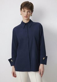 Navy button-up shirt with a pointed collar, long sleeves featuring gold starfish accents on cuffs, and a smooth texture.