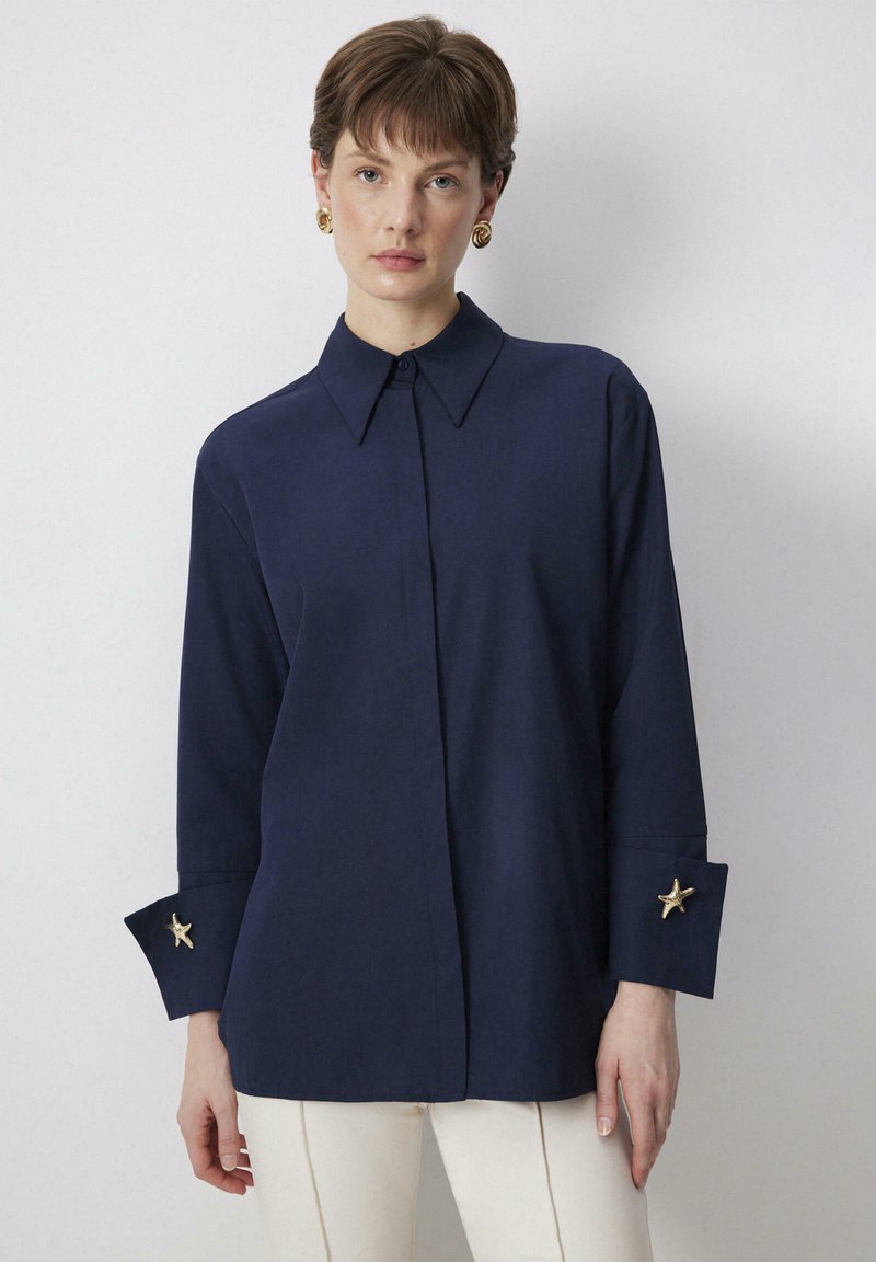 Navy button-up shirt with a pointed collar, long sleeves featuring gold starfish accents on cuffs, and a smooth texture.