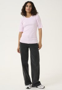 Ljusrosa ribbad t-shirt med korta ärmar, matchad med mörkgrå vida jeans och vita sneakers. Enkel design, inga mönster eller accenter.
