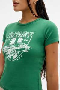 Zeleni pamučni majica s pripijenim dizajnom. Sadrži bijeli grafički print automobila i tekst "MOTOR CLUB DETROIT 1989" unutar štita.