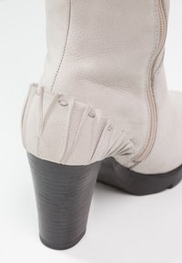 Jasnoszary skórzany botek za kostkę z żebrowanym detalem przy pięcie, fakturowaną powierzchnią oraz solidnym czarnym, masywnym obcasem.