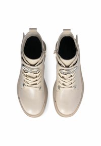 Beige leren enkellaarsjes met vetersluiting, metalen accenten en een rubberen zool. Voorzien van een trekhaak achter voor gemakkelijk aantrekken.