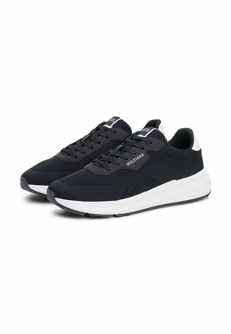 Zapatillas de punto en color azul marino con acentos en blanco y gris oscuro, que cuentan con un diseño de cordones y un patrón de tejido texturizado para mayor transpirabilidad.