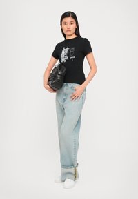 Svart bomull t-skjorte med hvit grafisk print; lyseblå høy midje-jeans; svart håndveske; hvite joggesko; avslappet passform og rette ben.