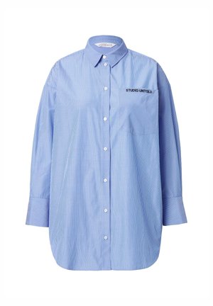 Camisa de botón a rayas azul con un bolsillo que presenta el texto "STUDIO UNTOLD", cuello clásico y mangas largas.