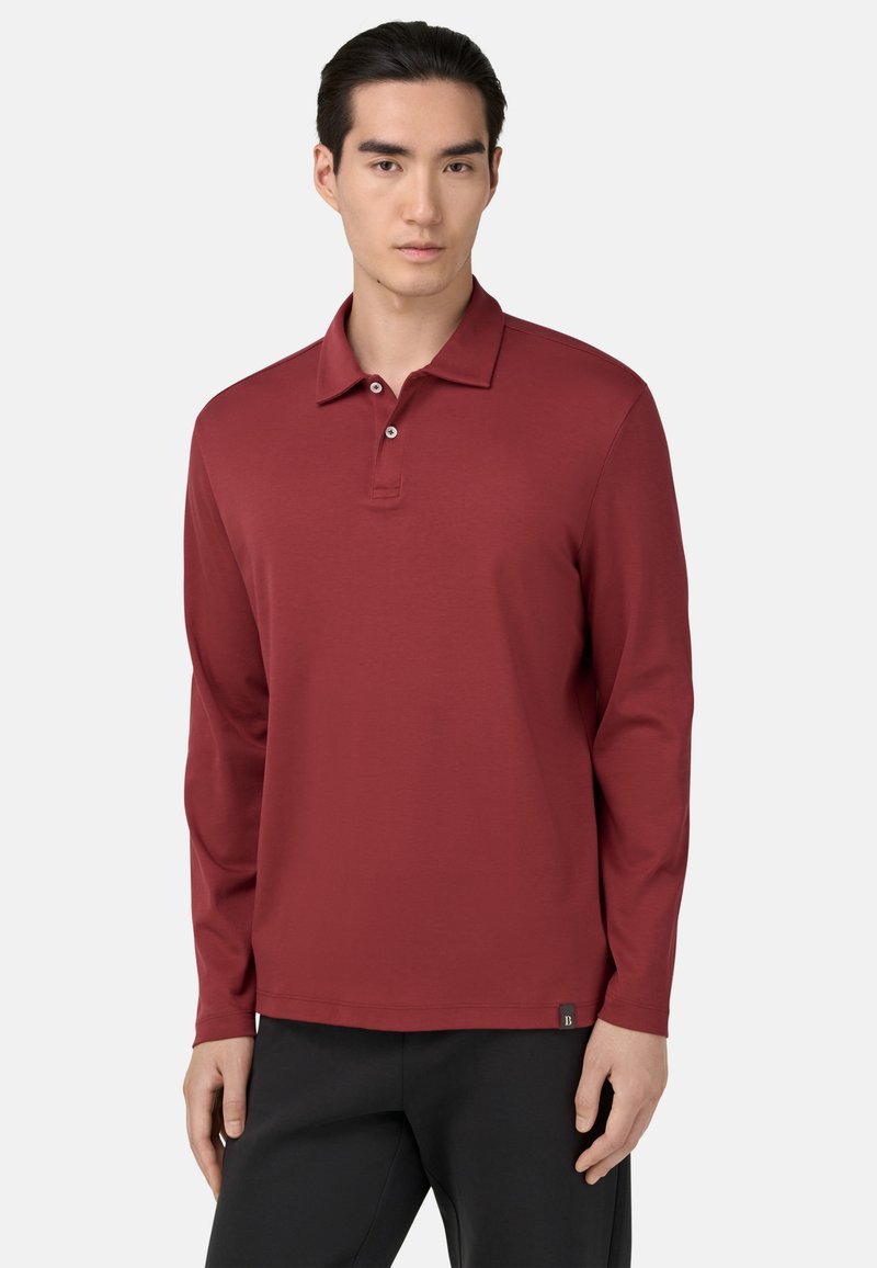 Raudona ilgomis rankovėmis polo marškinėliai, pagaminti iš minkštos medžiagos, su klasikiniais apykakle, dviejų mygtukų uždarymu ir maža logo detalė prie krašto.