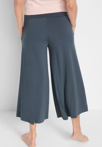 Pantaloni larghi realizzati in morbido tessuto grigio scuro con una texture liscia e vita elastica, dotati di tasche laterali e un fit rilassato.