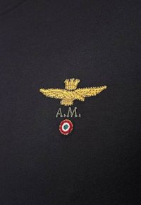 Tessuto nero con un'insegna di aquila ricamata in oro, testo 'A.M.' e un emblema rotondo con colori rosso, bianco e verde sottostante.