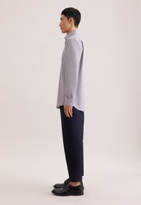 Camicia a maniche lunghe, azzurra a quadri, con bottoni, abbinata a pantaloni blu scuro e scarpe di pelle nere, vista di lato.