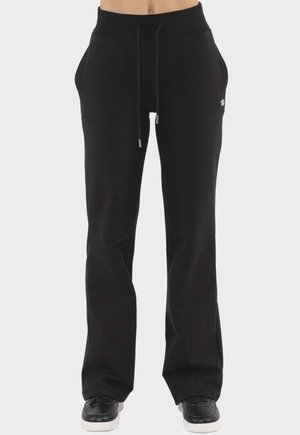 Femme portant un pantalon de jogging noir à jambes larges avec une taille à cordon et des poches, associé à des baskets noires avec des semelles blanches.