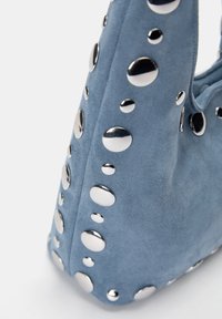 Geantă albastră din suede, ornamentată cu studuri metalice de diverse dimensiuni, evidențiind un design modern și elegant. Accent pe textură și embellishments.