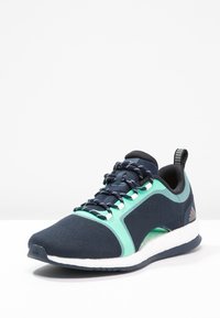 Scarpa da corsa blu navy con tomaia in mesh, dettagli verde menta, suola intermedia bianca e lacci motivo. Presenta un anello sul tallone per indossarla facilmente.