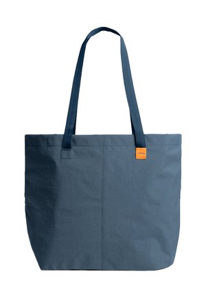 Borsa tote in tessuto blu scuro con manici lunghi e una piccola etichetta arancione vicino al bordo superiore su sfondo bianco.