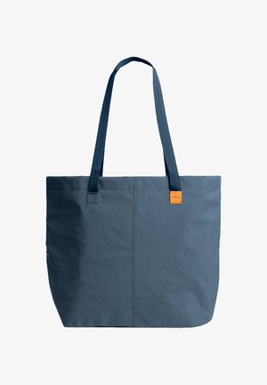 Sac fourre-tout en tissu bleu foncé avec de longues anses et une petite étiquette orange près du bord supérieur sur un fond blanc.
