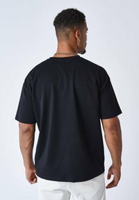 Camiseta negra de manga corta, hecha de algodón, con un corte relajado. Presenta un escote redondo y una textura suave. Sin patrones ni gráficos.