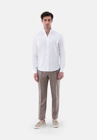 Camicia bianca a maniche lunghe con colletto alla cinese, abbinata a pantaloni sartoriali marrone chiaro e scarpe slip-on color crema.