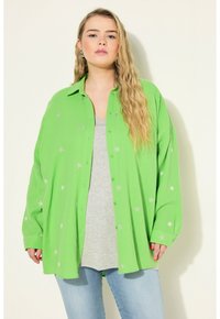 Zelená košile s knoflíky, s embosovanými stříbrnými hvězdnými vzory, texturovaná tkanina, uvolněný střih, nošena přes šedé tričko, spárovaná se světle modrými džíny.