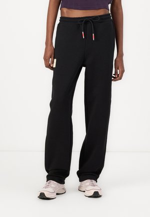 Black sweatpants made of soft fabric with a drawstring waist, straight-leg design, and a small label on the side. Paired with light sneakers.