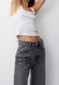 Top corto de canalé blanco y jeans de denim gris de tiro alto y corte holgado con un ligero desgaste, cierre de botón y cremallera, y diseño clásico de cinco bolsillos.