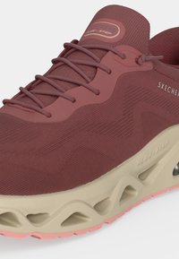 Близък план на бордо маратонка Skechers с връзки и светлобежова омекотена подметка с детайли с отвори и текстилна горна част с текстура.