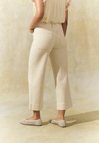 Beige cropped broek met een rechte pijpdesign, voorzien van twee achterzakken en een opgerolde zoom. Unieke gestructureerde schoenen maken de look compleet.