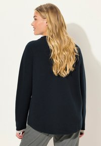 Suéter azul marino oscuro con cuello redondo, mangas largas y dobladillo curvado. Textura suave, con un detalle de puño en gris claro contrastante.
