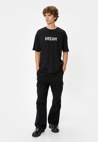 Musta lyhythihainen t-paita, jossa on edessä hopeinen "DREAM" -teksti, yhdistettynä mustiin cargo-housuihin ja mustiin kenkiin. Yksinkertainen, rento muotoilu.