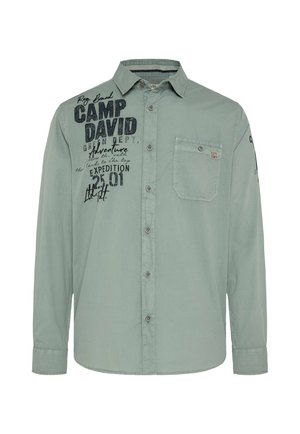 Lange mouwen shirt van lichtgroene stof met een kraag, voork pocket en donkere bedrukte tekstdetails. Bevat knoopsluitingen en manchetten.