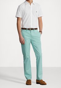 Polo shirt bianco a maniche corte, chinos azzurri chiari, cintura di cuoio marrone e mocassini marroni. Design semplice con taglio e colori classici.