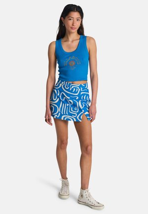 Blauw nauwsluitend tanktopje met een logo en een witte mini-rok met abstracte blauwe en witte patronen, met een gelaagd ontwerp en een zijsplit.