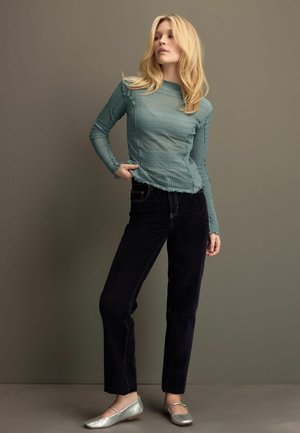Een langmouwen getextureerde teal top met gestreept patroon, gecombineerd met donkere slim-fit jeans en zilveren platte schoenen. Eenvoudig, gelaagd ontwerp.