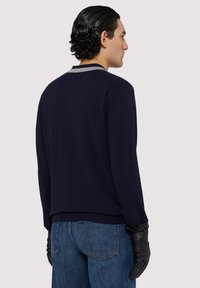 Maglione lavorato a maglia blu navy con colletto grigio chiaro, bordo a coste e maniche lunghe, abbinato a jeans in denim blu scuro e guanti neri.