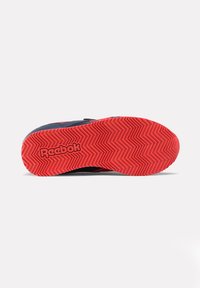 Zapato Reebok con suela de goma con un patrón de zigzag en rojo y parte superior negra. Detalle de cinta de velcro para un ajuste seguro.